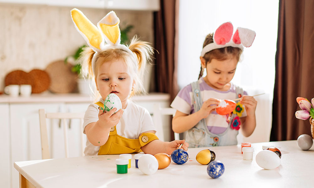 Two small girls in a kitchen eating Easter eggs