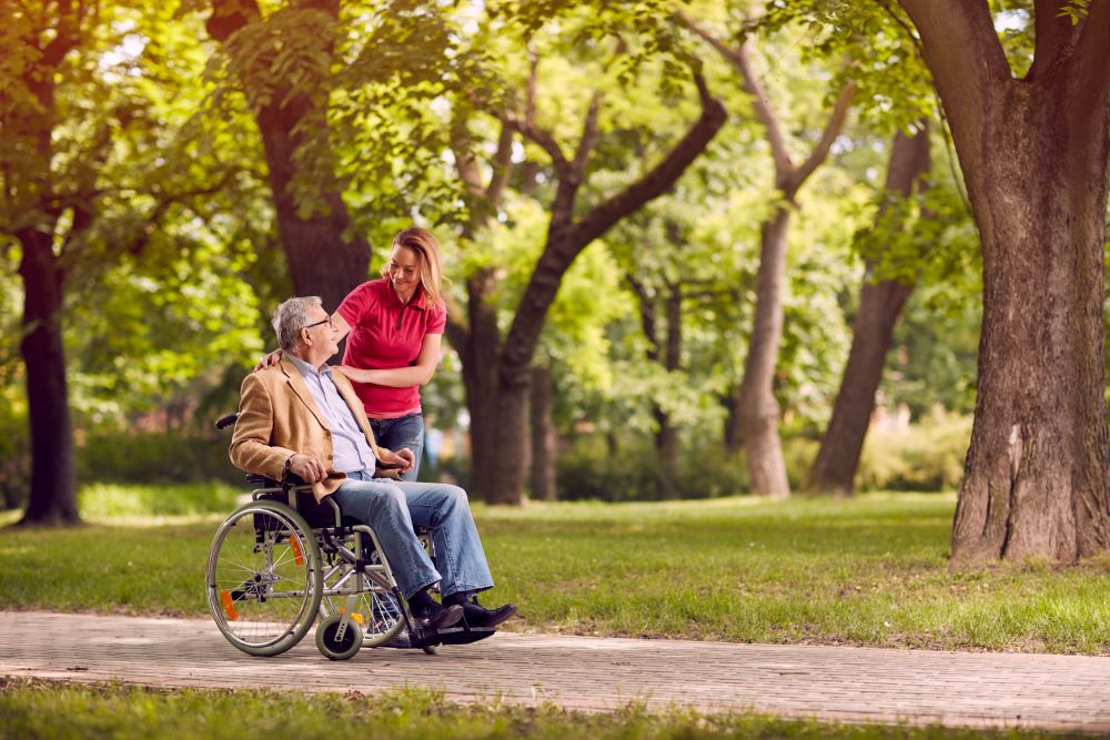 Male in a wheelchair in a park setting with a younger female caring Male in a wheelchair in a park setting with a younger female caring