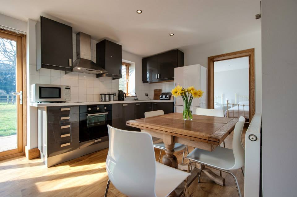 hollambys-cottages An interior shot of a small kitchen with a dining table and two chairs with a door leading into a bedroom in the background