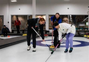 Group of 3 people curling, with 2 brushing the ice